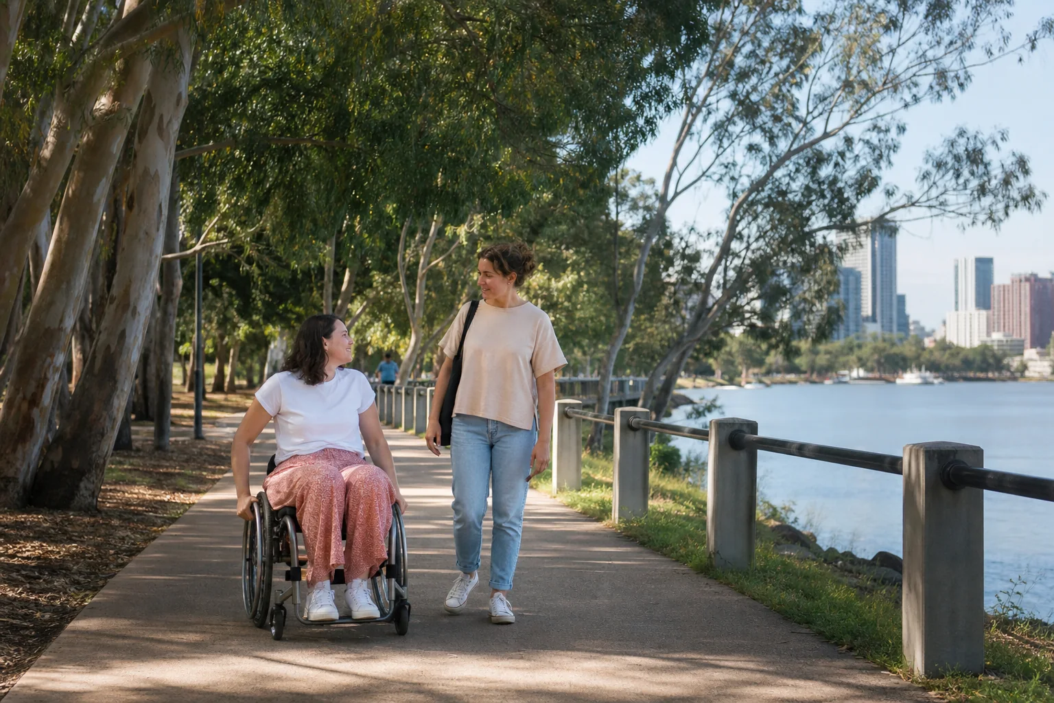 An adult wheelchair user and support worker moving together on a Brisbane riverside path